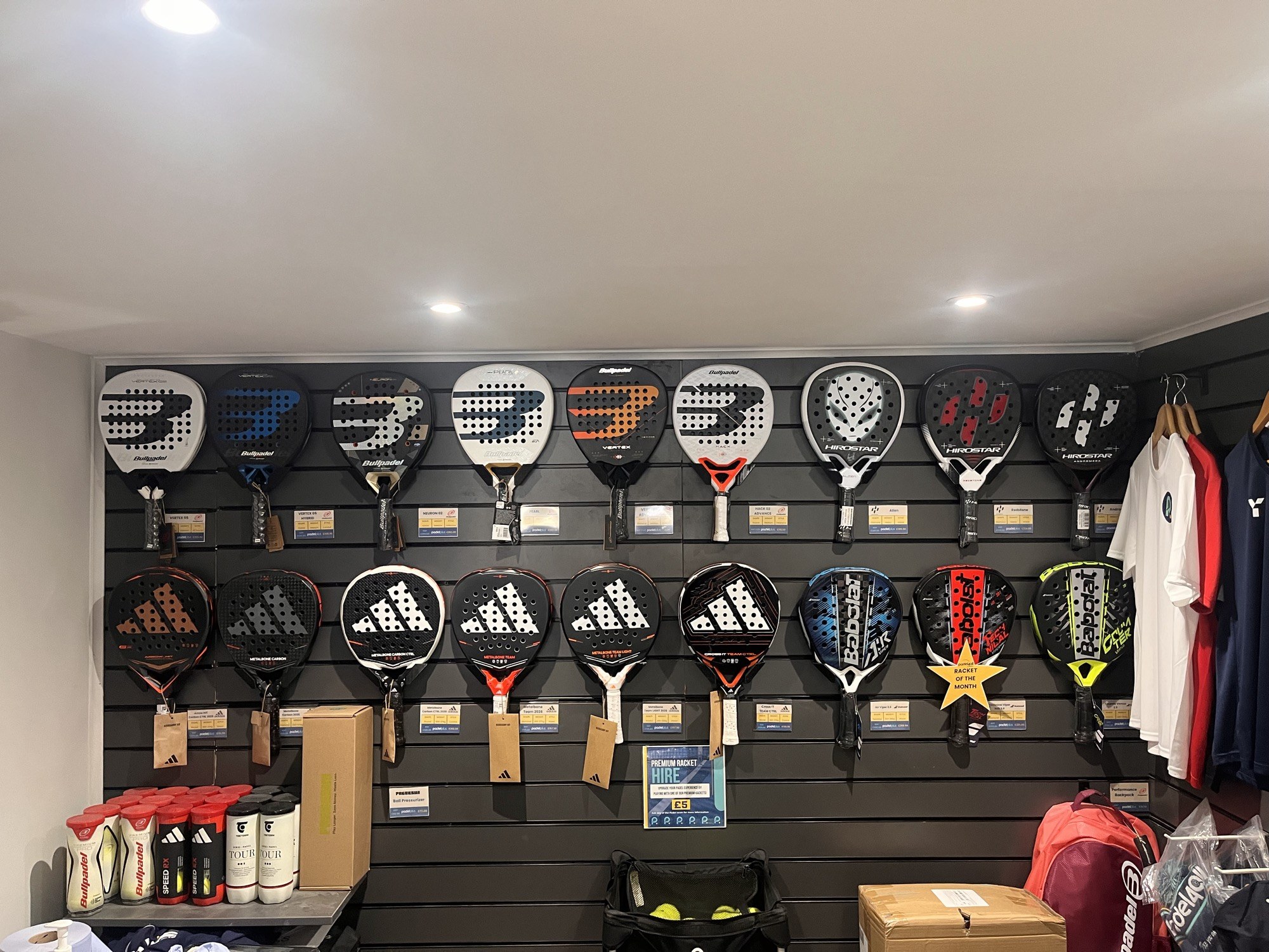 A padel club shop wall hung with rackets in two rows above price tags