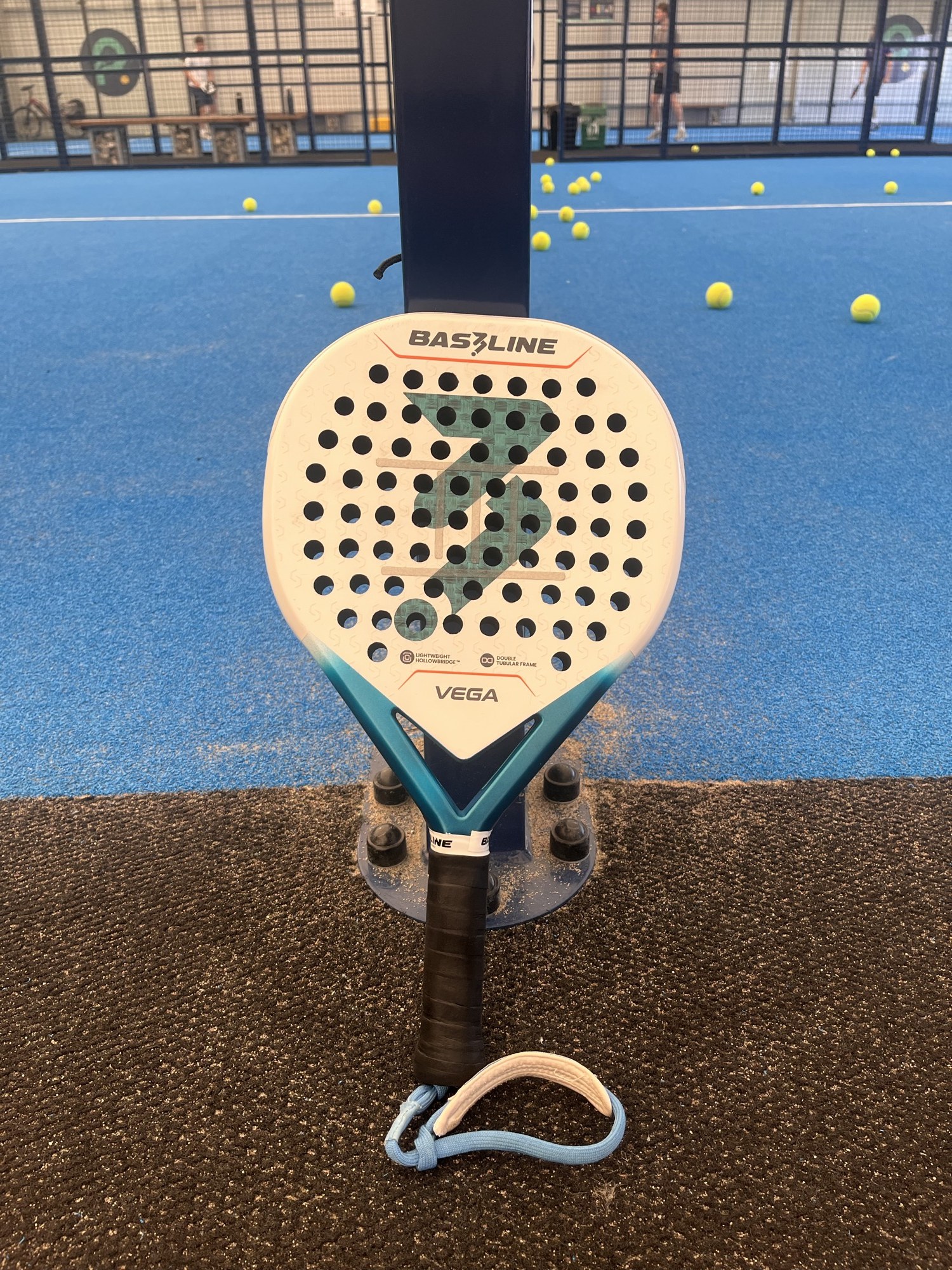A single Bas3line Vega racket resting on a court net post