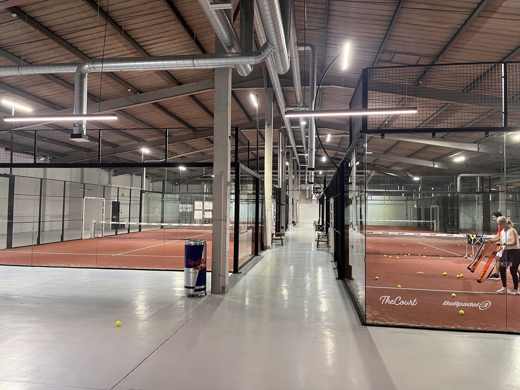 A polished walkway running between glass-walled indoor padel courts