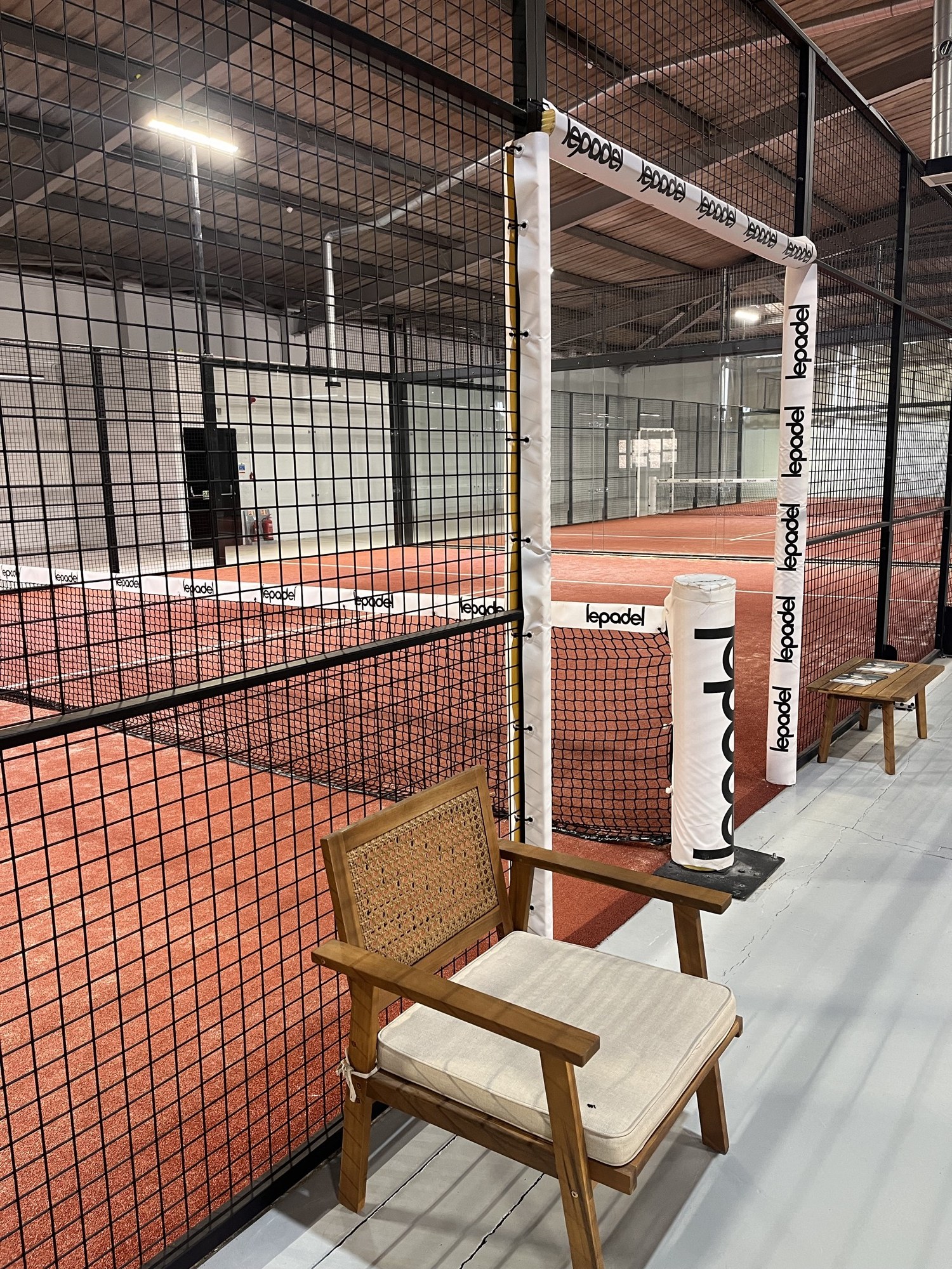 Indoor padel courts behind glass with a cane armchair at the court's edge