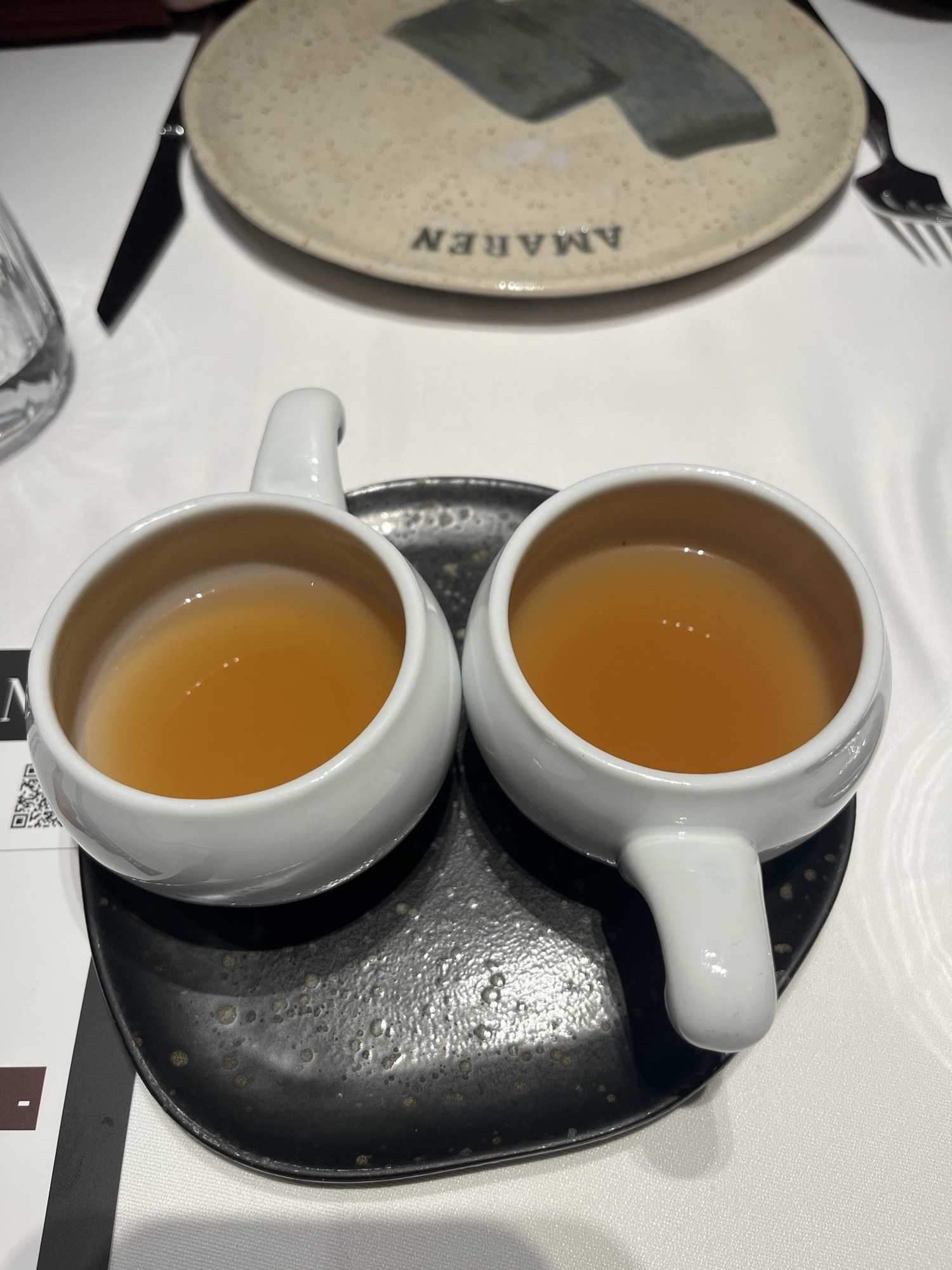 Two cups of amber bone broth on a black plate