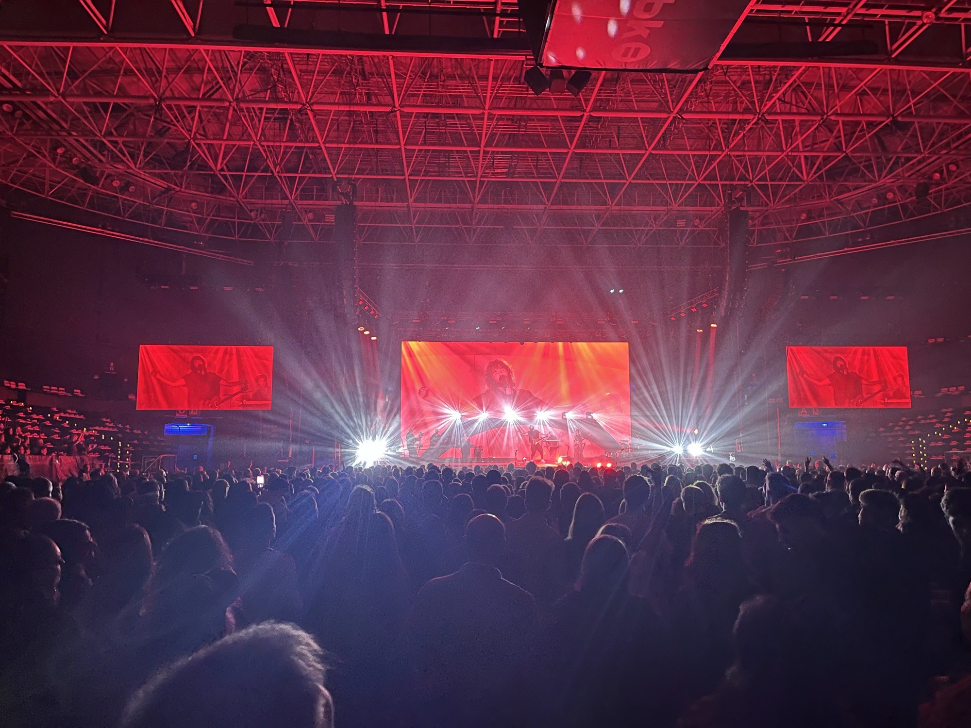 A concert at the Bilbao Arena, the room lit red, the performer on three screens