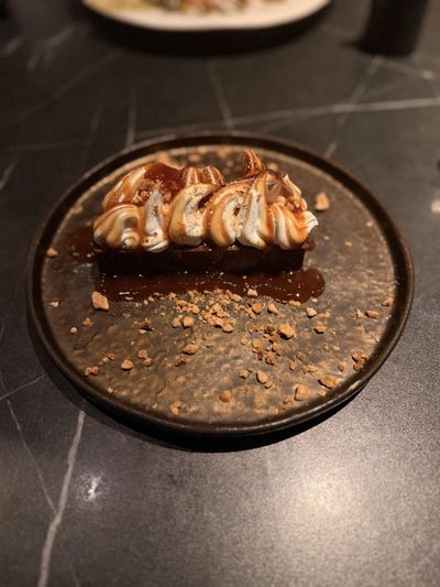 A chocolate bar under piped, torched meringue on a dark plate, scattered with peanut crumble