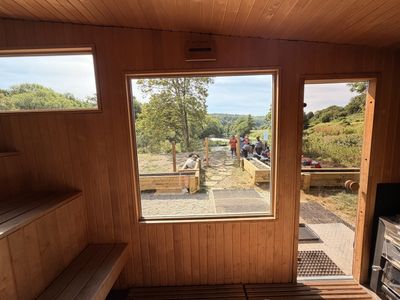 Inside the sauna, timber benches and a stove, with a picture window looking out to the river