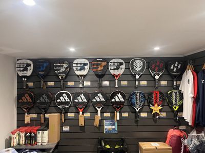 A padel club shop wall hung with rackets in two rows above price tags