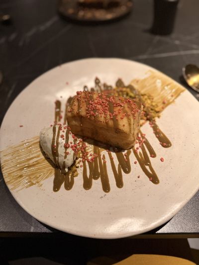 A torrija with pistachio cream, pink sugar pearls and ice cream on a white plate