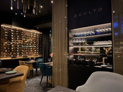A dark dining room with a lit wine wall, velvet chairs and the OCULTO wordmark