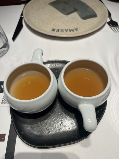 Two cups of amber bone broth on a black plate