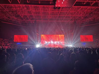 A concert at the Bilbao Arena, the room lit red, the performer on three screens