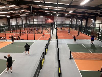 Pickleball courts in the foreground and padel courts behind glass, both in use
