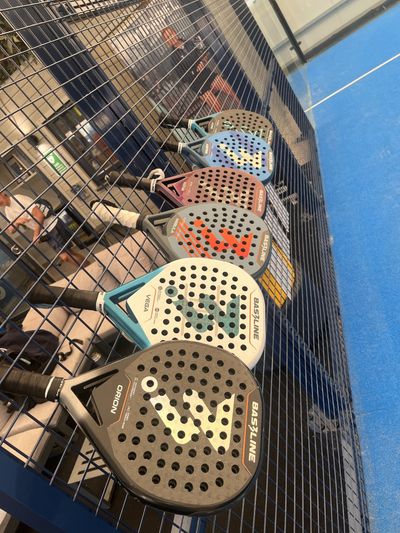 Six Bas3line teardrop rackets hung in a row on a court fence
